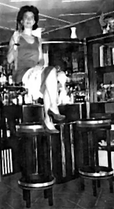 Yoganne, la fille de Yogano, assise en hauteur au-dessus des tabourets d’un bar, dans le numéro du Diabolo Bar